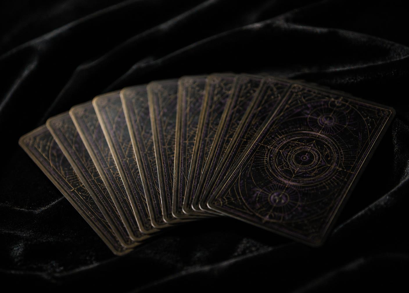 Antique oracle and tarot cards fanned across black velvet in low violet light
